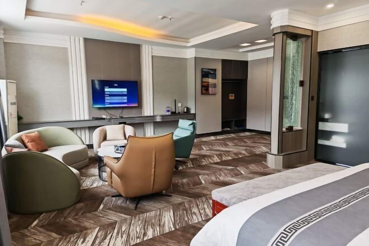 Quarto de hotel com cama, secretária com computador, televisão e área de estar com cadeiras.