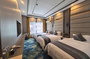 A hotel room with three beds, a TV, a minibar, and a large window with curtains.
