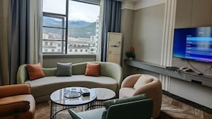 Moderni hotellihuone, jossa on kaareva sohva, pieni pyöreä pöytä ja seinälle asennettu televisio.