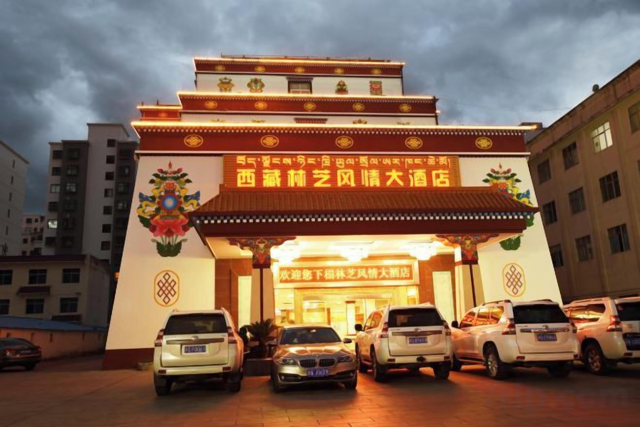 A hotel entrance with a traditional architectural design, featuring a prominent entrance gate and a parking area with several cars.