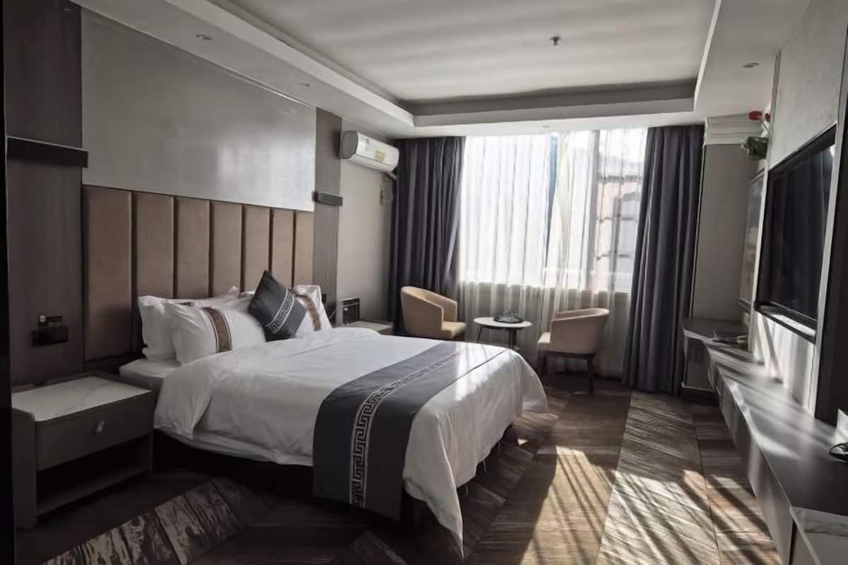 Quarto de hotel com uma cama grande, mesa de cabeceira, uma cadeira, uma mesinha e uma televisão.