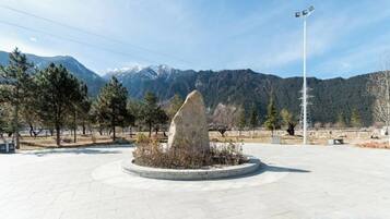 A circular plaza with a central stone monument, surrounded by trees and a mountain backdrop.