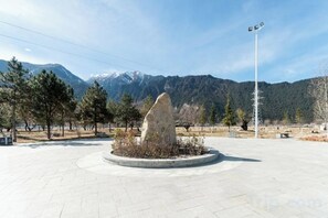 Una plaza circular con un monumento de piedra en el centro, rodeada de árboles y con una montaña al fondo.