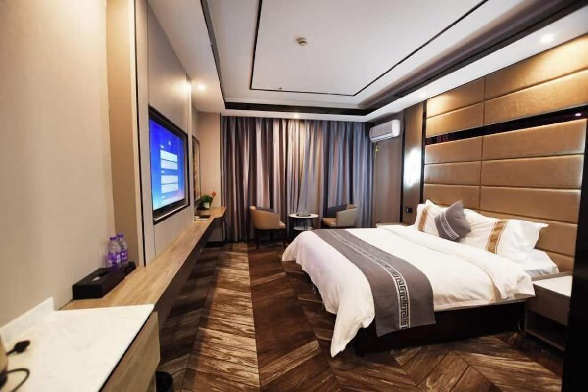 Quarto de hotel moderno com uma cama grande, uma escrivaninha, uma televisão e um espaço de estar com cortinas.
