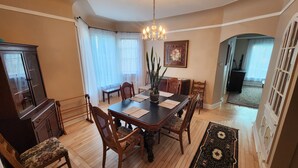 Une salle à manger avec une table en bois foncé, six chaises, un lustre et une grande fenêtre ornée de rideaux légers.