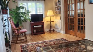 Un salon comprenant un téléviseur, un fauteuil à bascule, une table basse en verre et un tapis à motifs.