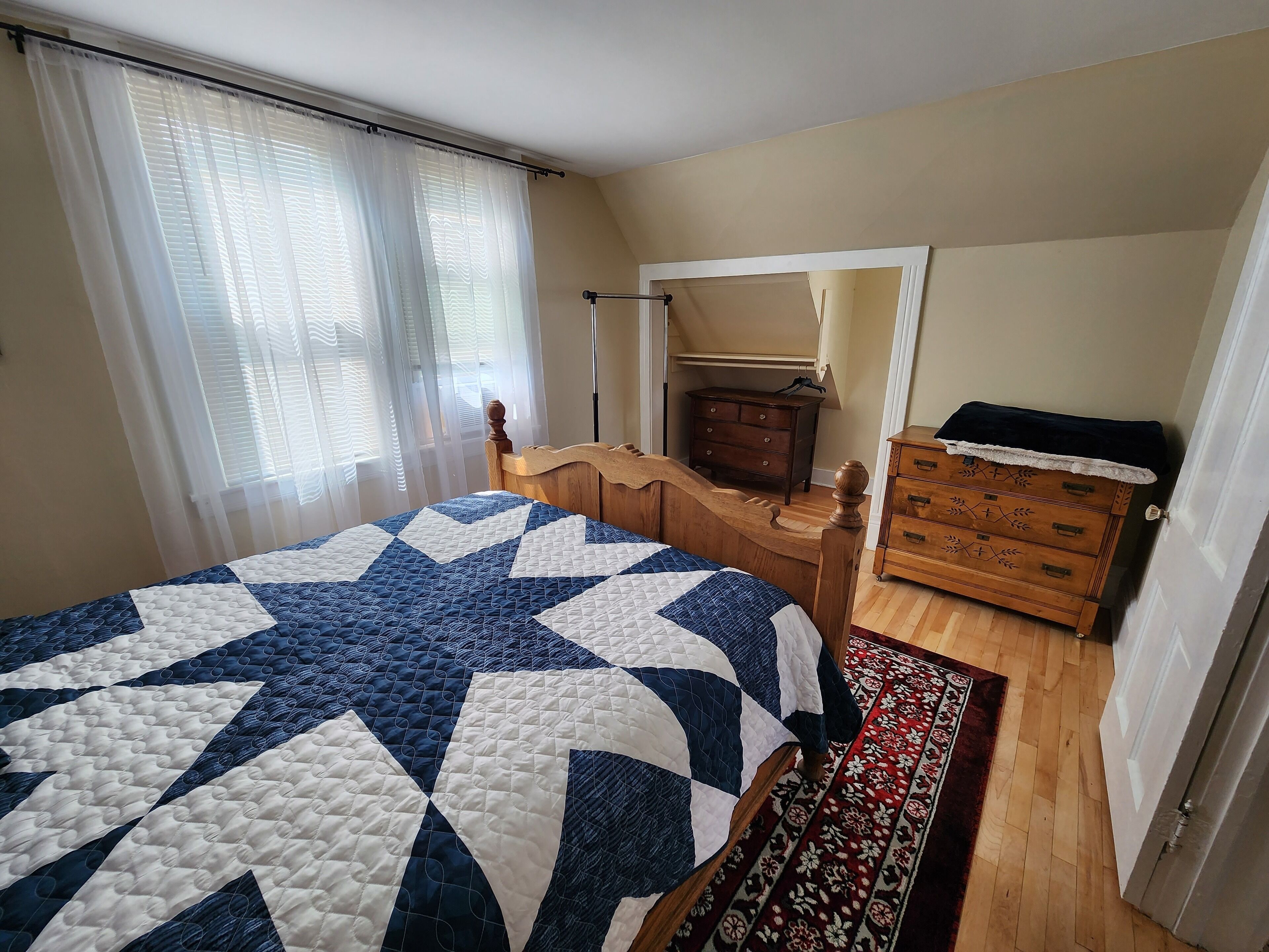 Una camera da letto con un letto grande, una cassettiera in legno, uno specchio e una finestra con tende leggere.