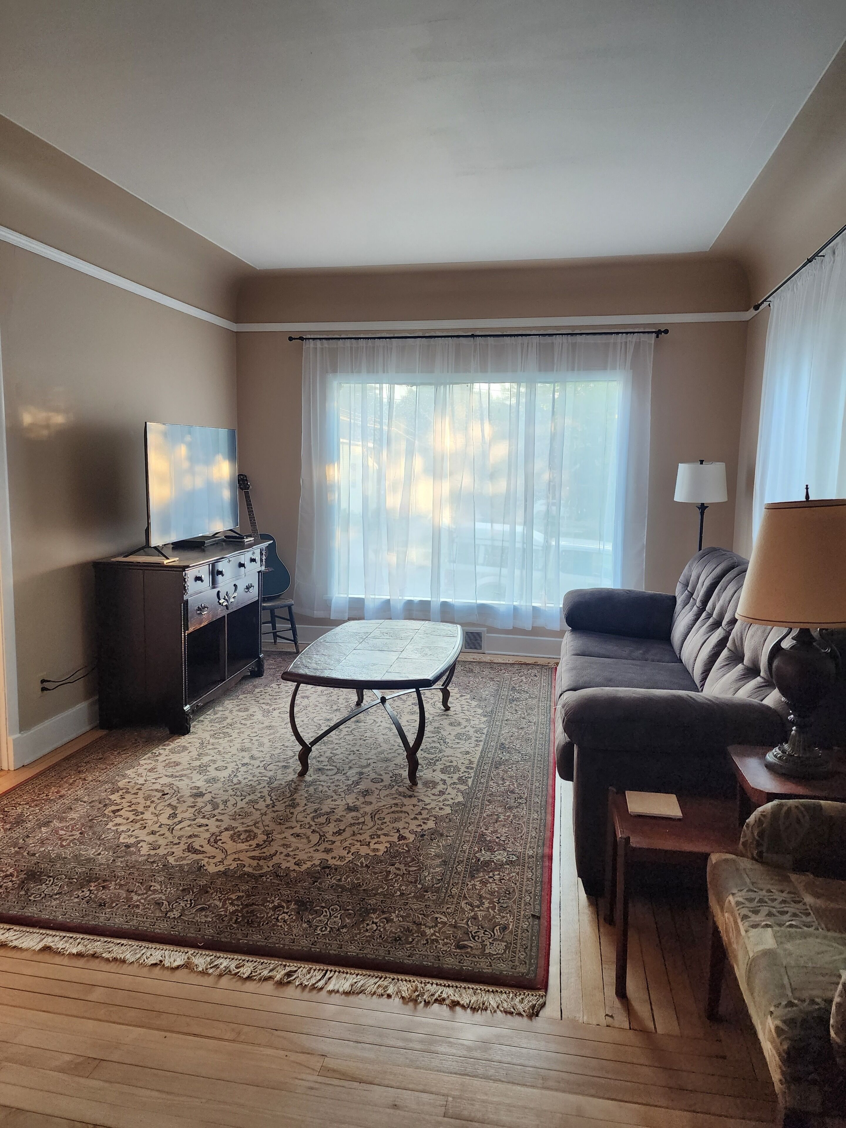 A living room with a television, a guitar, a sofa, a lamp, and a patterned rug.