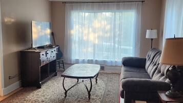 A living room with a television, a guitar, a sofa, a lamp, and a patterned rug.