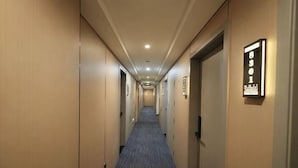 A hotel hallway with doors on both sides, a carpeted floor, and a sign with numbers on the wall. - Harmony One Hotel (Enshi City)
