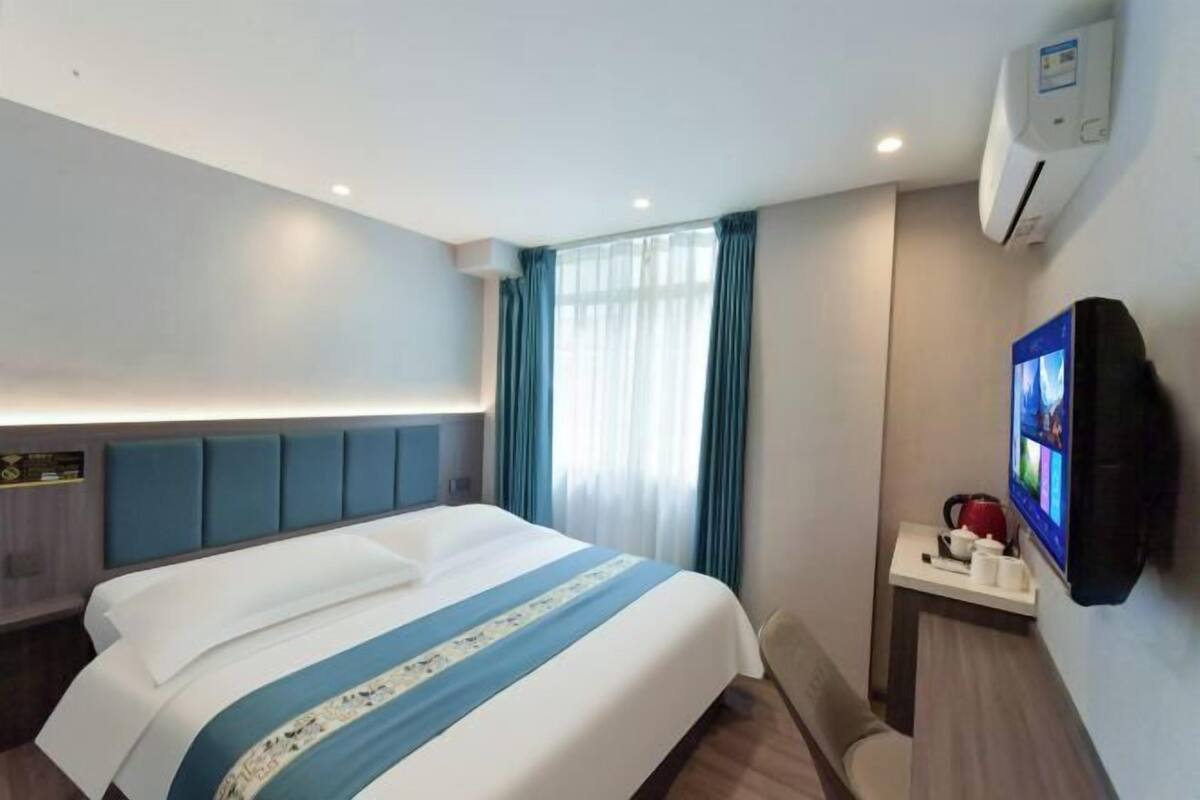 Ein Hotelzimmer mit einem Bett, einem kleinen Tisch mit Wasserkocher, einem Fernseher und einer Klimaanlage.