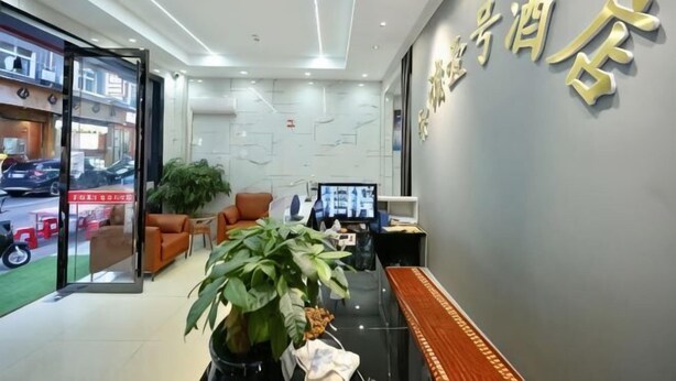 A hotel reception area with a reception desk, seating area, and a large plant. - Harmony One Hotel (Enshi City)