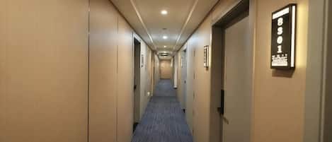 A hotel hallway with doors on both sides, a carpeted floor, and a light fixture on the wall.