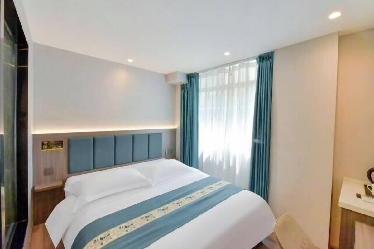 Ein Hotelzimmer mit Bett, Nachttisch, Schreibtisch und einem Fenster mit Vorhängen.