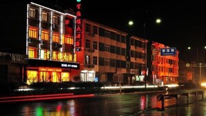 A multi-story building with illuminated signage, a wet street reflecting lights, and a clear view of the building's facade. - Wangyanlou Hotel (Yueqing)