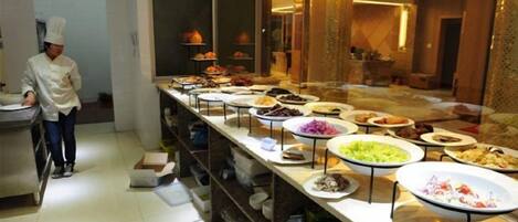 A buffet setup with various dishes and a chef in the background.