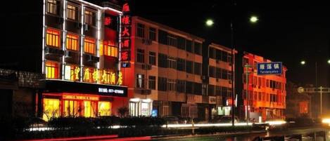 A multi-story building with illuminated signage, a wet street reflecting lights, and a clear night sky.
