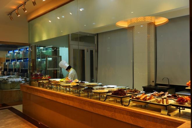 A buffet setup with a chef preparing food, a variety of dishes displayed, and a modern interior design.