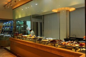 A buffet setup with a chef preparing food, a variety of dishes displayed, and a modern interior design. - Wangyanlou Hotel (Yueqing)