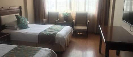 A hotel room with two beds, a TV, a desk, and a window with curtains.