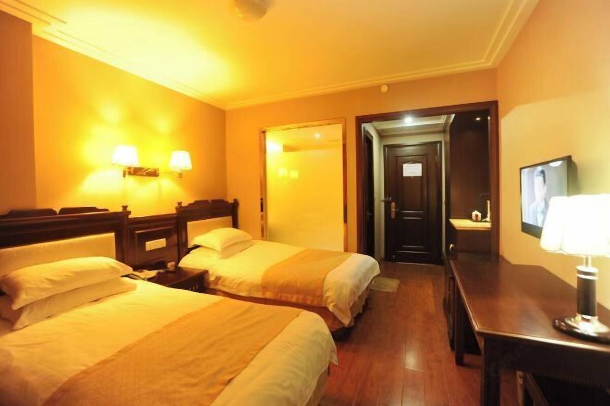 Une chambre d’hôtel avec deux lits, un bureau, une télévision et une porte donnant sur une autre chambre.