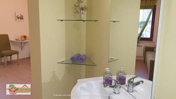 A bathroom with a white sink, two glass shelves, and a mirror. There are two purple towels on the middle shelf and two bottles of soap on the bottom shelf.