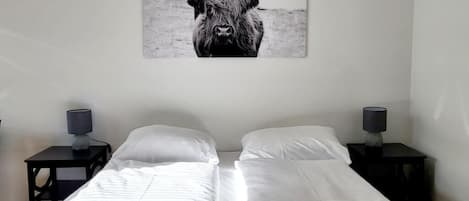 Habitación de hotel con dos camas, ropa de cama blanca y una fotografía grande en blanco y negro de un toro en la pared.