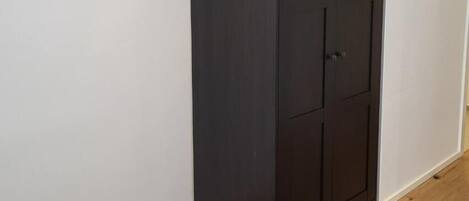Un armario oscuro contra una pared blanca con suelo de madera.