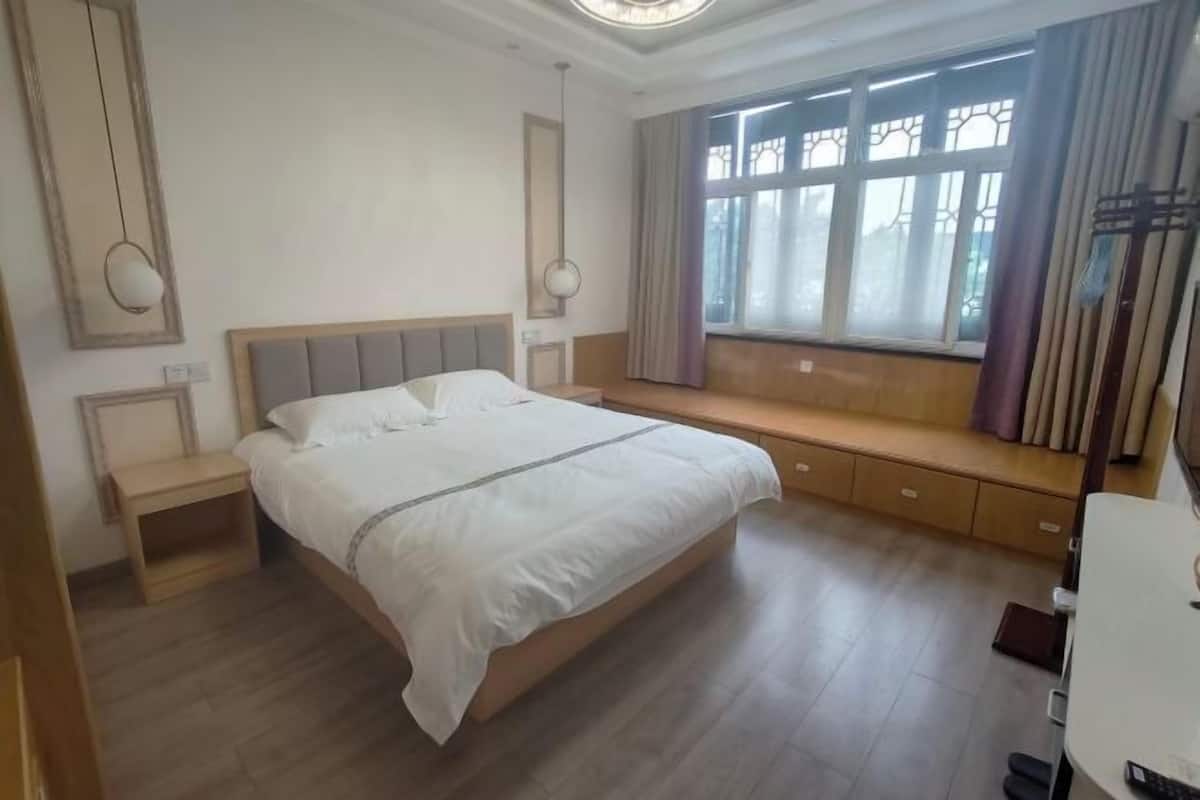 Een slaapkamer met een bed, nachtkastjes, een raam met gordijnen en een bureau met stoel.