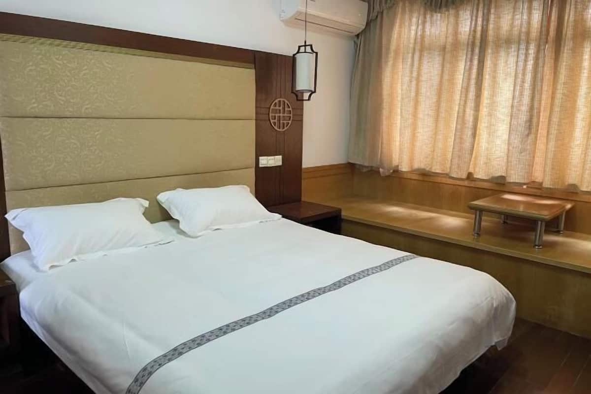 Een hotelkamer met een groot bed, een nachtkastje, een klein tafeltje, een wandlamp en een raam met gordijnen.