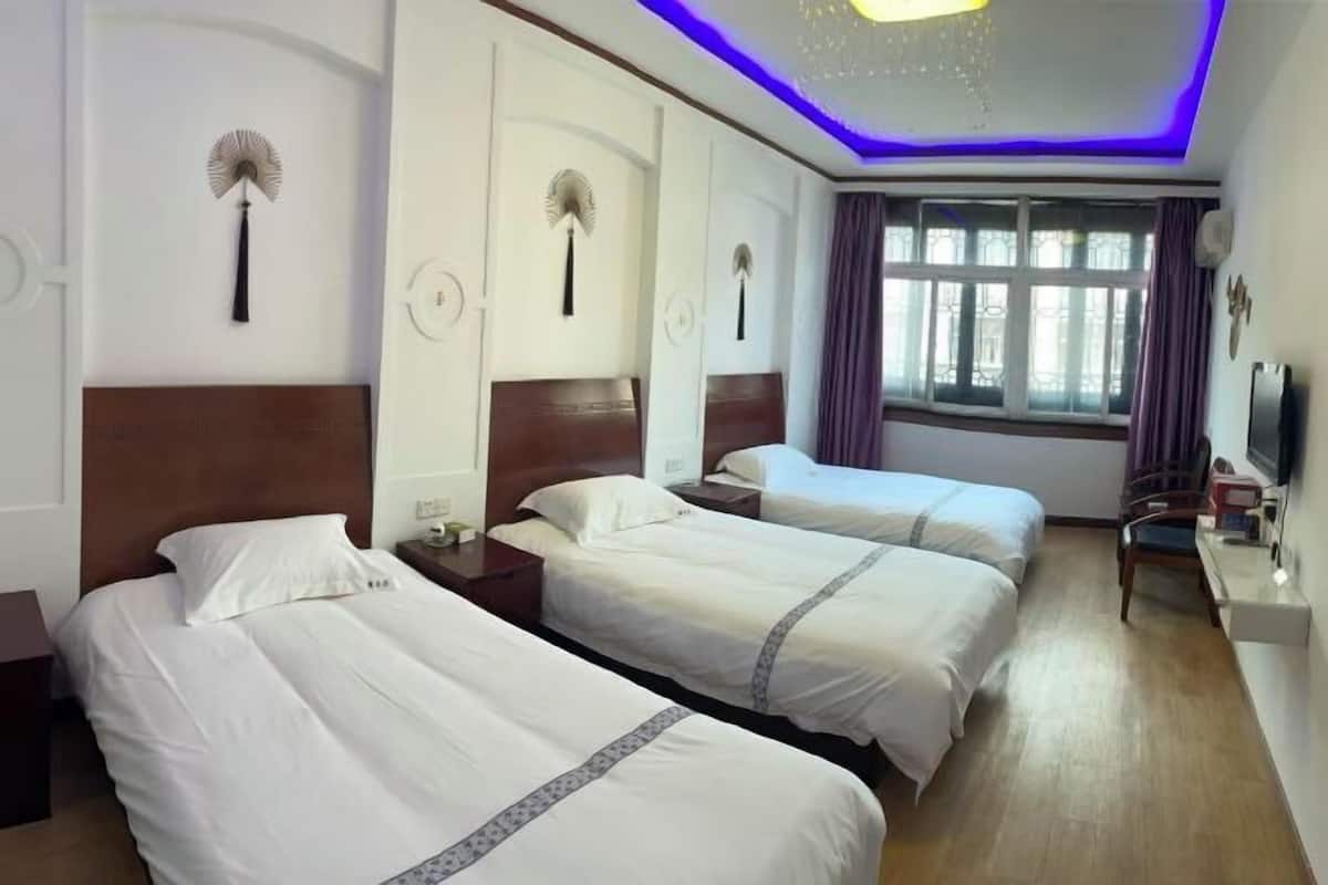 Een hotelkamer met drie bedden, een bureau, een stoel en een raam met gordijnen.