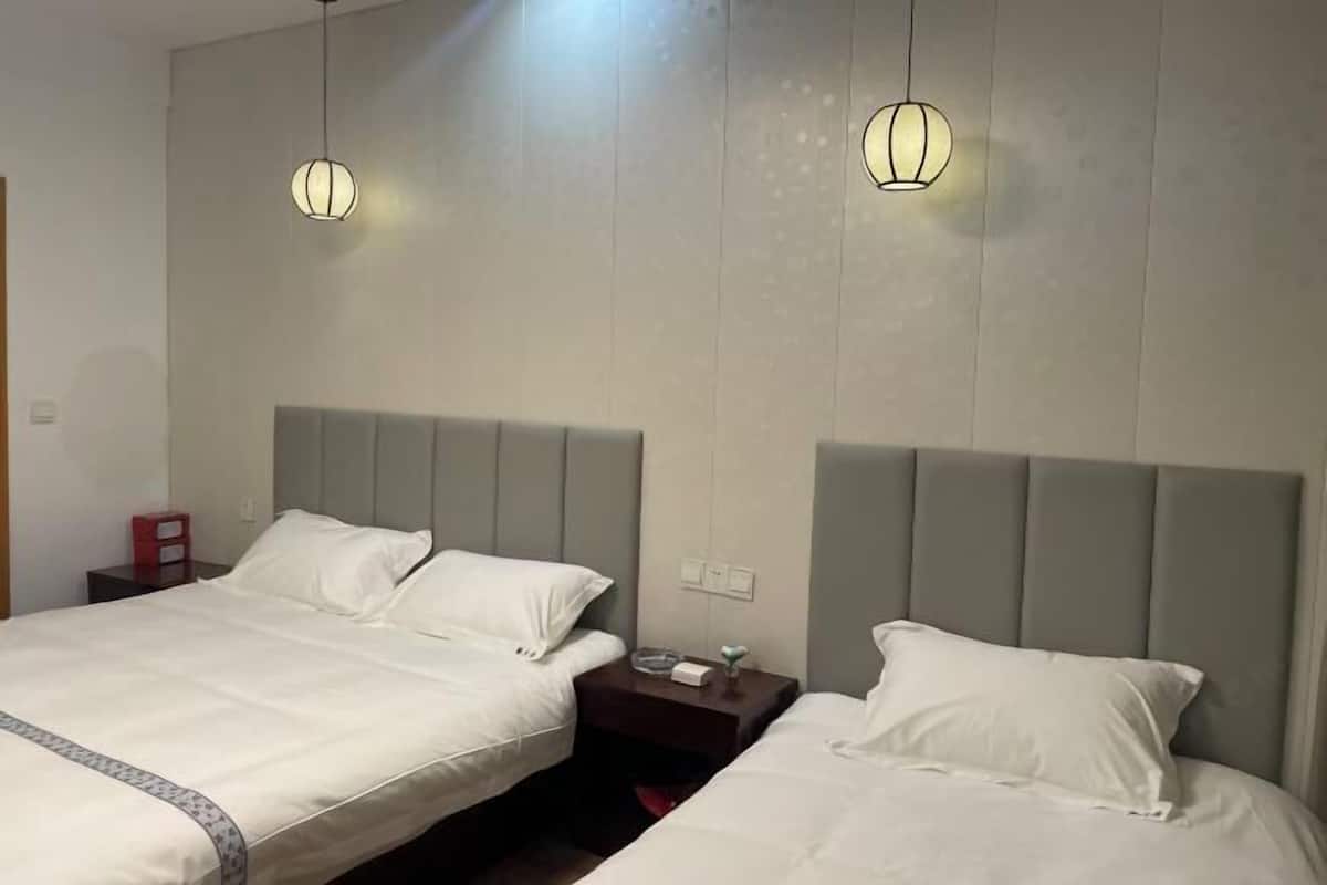 Een hotelkamer met twee bedden, elk voorzien van wit beddengoed en hoofdborden. Er zijn twee nachtkastjes met lampen en een kleine rode doos op één van de nachtkastjes.