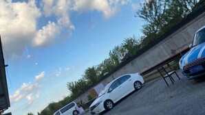 Ένας χώρος στάθμευσης με αρκετά αυτοκίνητα, ένας τοίχος από σκυρόδεμα και ένας καθαρός ουρανός με σύννεφα.