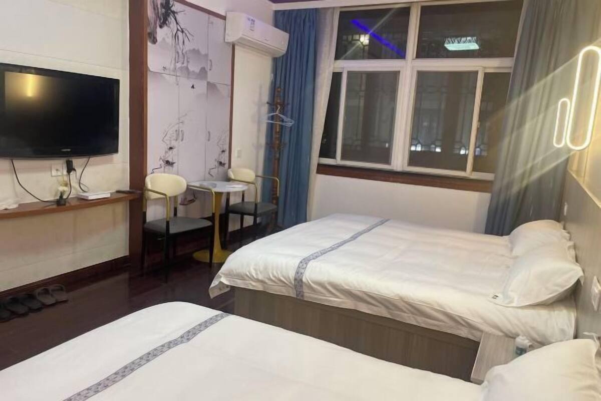 Een hotelkamer met twee bedden, een televisie, een bureau en een raam met gordijnen.