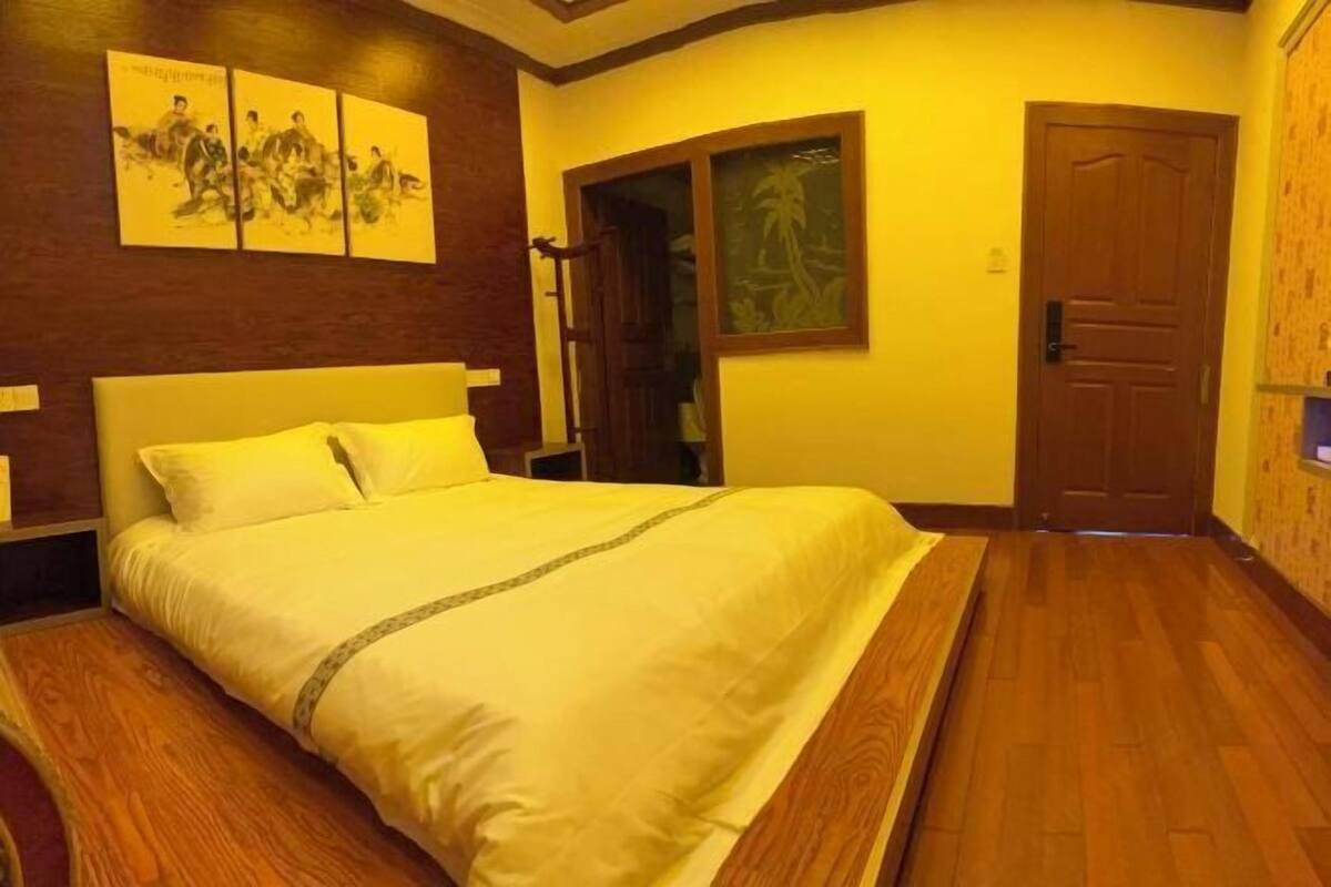 Hotelkamer met een groot bed, houten vloer, een houten hoofdbord en kunstwerken aan de wanden.