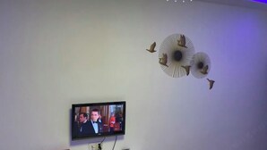 Μια τηλεόραση τοποθετημένη στον τοίχο, με ένα διακοσμητικό φωτιστικό οροφής και μια μικρή λευκή κονσόλα από κάτω.