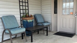 Un porche avec deux chaises, une table et un paillasson.