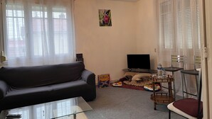 A living room with a black sofa, a glass coffee table, a TV, and a small wooden table with chairs. - Maison Carpe Diem Maximum Pour 4 Personnes (Romilly-sur-Seine)
