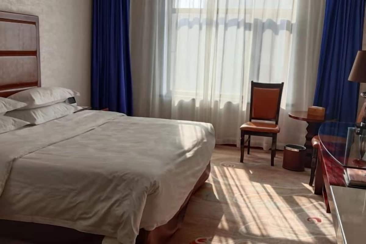 A hotel room with a bed, a chair, a small table, and a lamp.