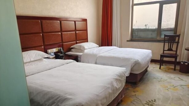 A hotel room with two beds, a wooden headboard, a window with curtains, and a floral carpet. - Wulate Hotel (Urad Front Banner)