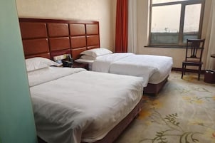 Habitación de hotel con dos camas, cabecero de madera, ventana con cortinas y alfombra estampada.