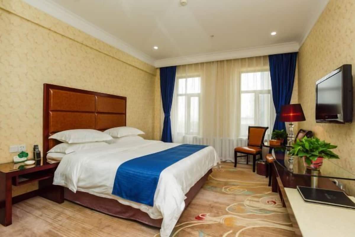 A hotel room with a bed, a desk, a chair, a TV, and a window with curtains.