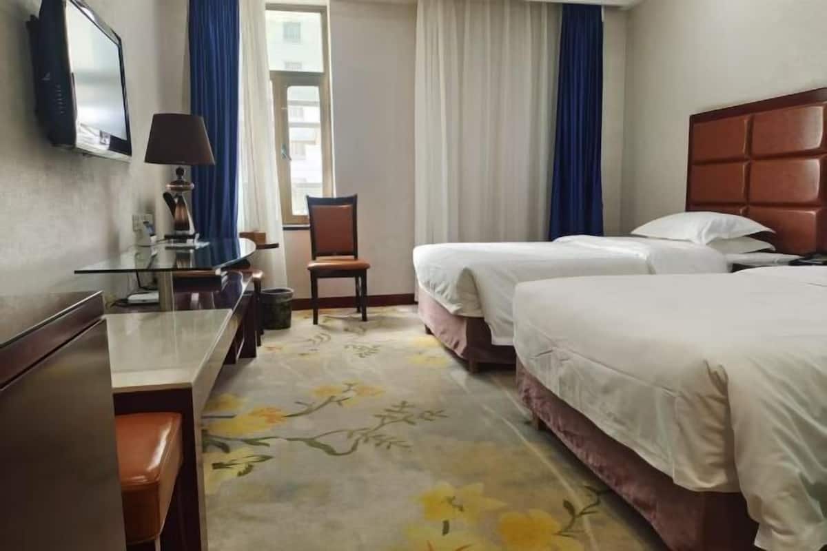 A hotel room with two beds, a desk with a lamp, a TV, and a window with curtains.