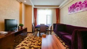A hotel room with a television, a dining table, a sofa, and a patterned carpet. - Wulate Hotel (Urad Front Banner)