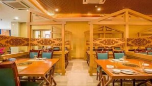 A restaurant with wooden tables and chairs, a central aisle, and decorative panels on the walls. - Wulate Hotel (Urad Front Banner)