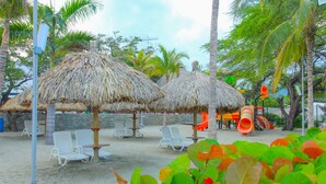A beachside area with thatched umbrellas, white lounge chairs, and a playground. - Super Apartamento Familiar - Samaria Club Playa (Santa Marta)