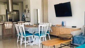 A dining area with a checkered tablecloth, white chairs with teal cushions, a wooden bench, and a TV mounted on the wall. - Super Apartamento Familiar - Samaria Club Playa (Santa Marta)
