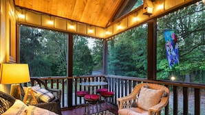 Un espace extérieur abrité, aménagé avec des meubles en osier, une table avec des coussins rouges et une vue sur une forêt.