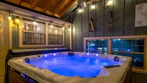 Un bain à remous avec un éclairage bleu, des murs en bois et des fenêtres équipées de stores.