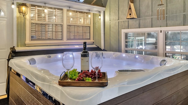 Un bain à remous avec un plateau en bois rempli de raisins et deux verres, une bouteille de vin, et une nichoir en bois accroché au mur.